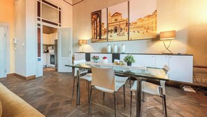 A modern kitchen with a dining area, featuring a glass table, white chairs, and a large cityscape painting on the wall.