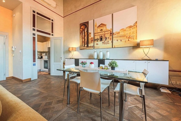 A modern kitchen with a dining area, featuring a glass table, white chairs, and a large cityscape painting on the wall. - Ricasoli Terrace (Florence)