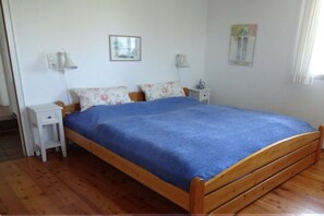 Einzimmerappartement mit einem Bettgestell aus Holz, einer blauen Bettdecke, zwei Nachttischen mit Lampen und einem kleinen weißen Beistelltisch.