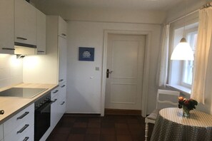 A kitchen with white cabinets, a stove, and a dining area with a table and chairs. - Holiday home in Oldsum with swimming pool (Oldsum)