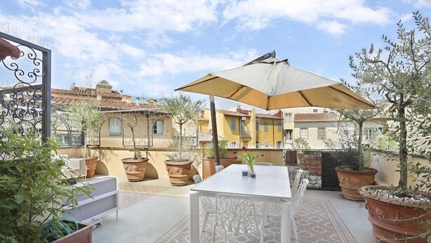 An outdoor patio with a table and chairs, surrounded by potted plants and a decorative metal fence. - Luxury Apartment in Central Florence (Florence)