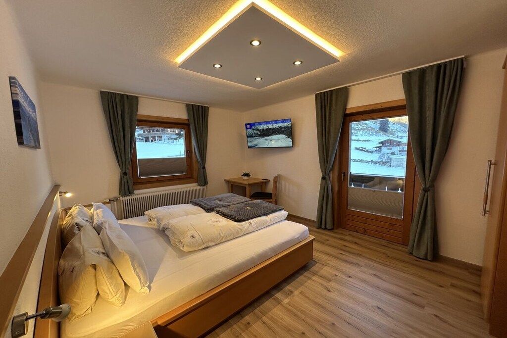 A bedroom with a bed, a television, and a window with curtains.