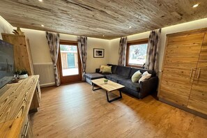 Een woonkamer met een houten plafond, een bank, een salontafel en een houten kast.