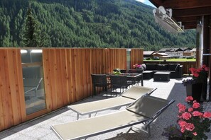 An outdoor patio with wooden walls, a table with chairs, and lounge chairs. - Holiday apartment with 1 bedroom (St. Jakob)