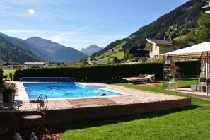 A swimming pool with a view of mountains, a grassy area, and a building with a covered patio. - Holiday apartment with 1 bedroom (St. Jakob)