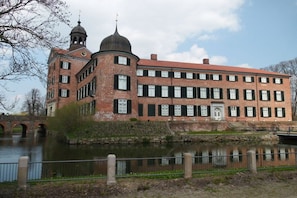 En historisk byggnad i tegel med en central kupol och en bro i bakgrunden.