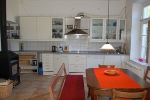 A kitchen with white cabinets, a stove, a dining table with a red tablecloth, and a window. - Old Rectory Elmenhorst (Elmenhorst)