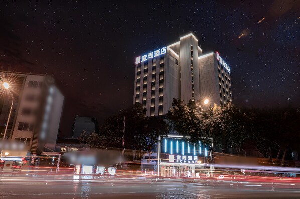 A high-rise hotel with illuminated signage, a parking lot, and a street with light trails. - Echarm Hotel (Mianyang)
