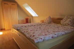 Quarto com teto inclinado, cama com roupa de cama floral, guarda-roupa de madeira e um claraboia.
