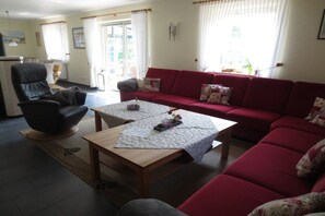 A living room with a red sofa, a wooden coffee table, a black armchair, and a small table with a vase of flowers. - | Friesenhaus Deichperle (St. Peter-Ording)