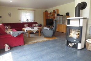 A living room with a red sofa, a grey armchair, a television, and a fireplace. - | Friesenhaus Deichperle (St. Peter-Ording)