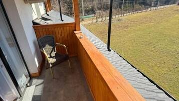 Un balcon en bois donnant sur une zone verdoyante et des arbres. On y trouve deux chaises en osier et une petite table.
