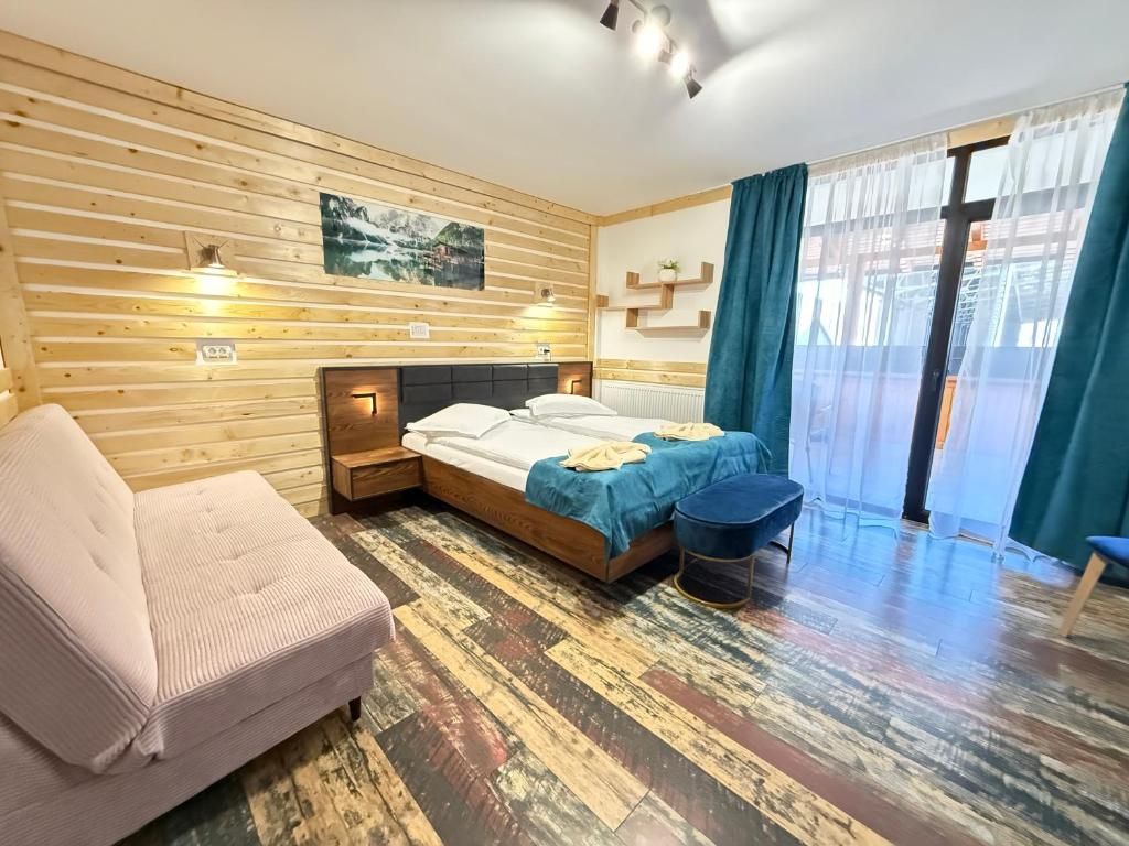Una habitación con pared de listones de madera, cama con colcha azul, sofá rosa y una pequeña mesa redonda.