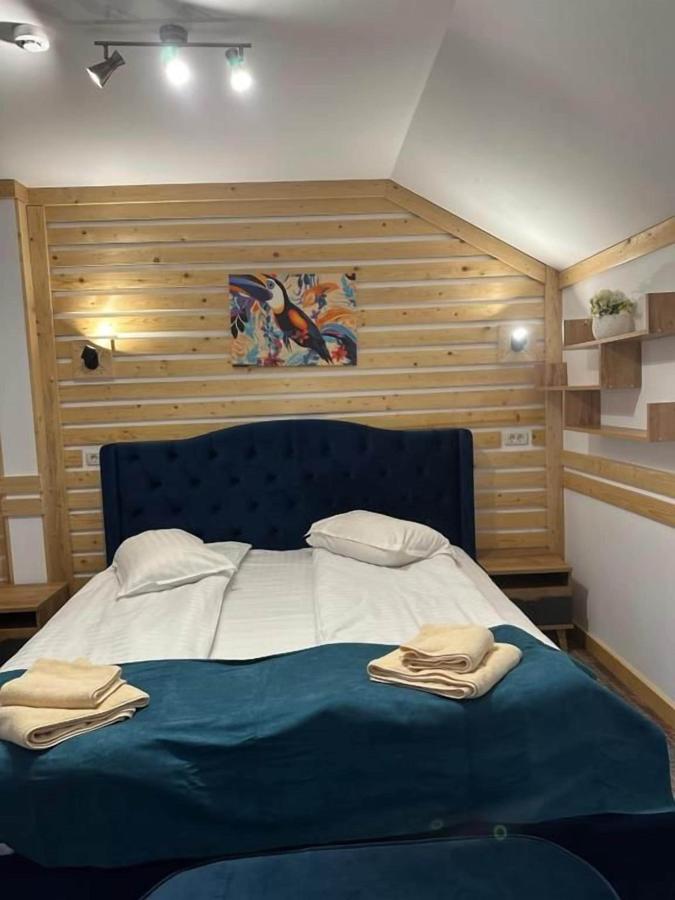 A hotel room with a bed, a wooden headboard, a painting, and a shelf with a plant.