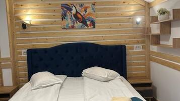 A hotel room with a bed, a wooden headboard, a painting, and a shelf with a plant.