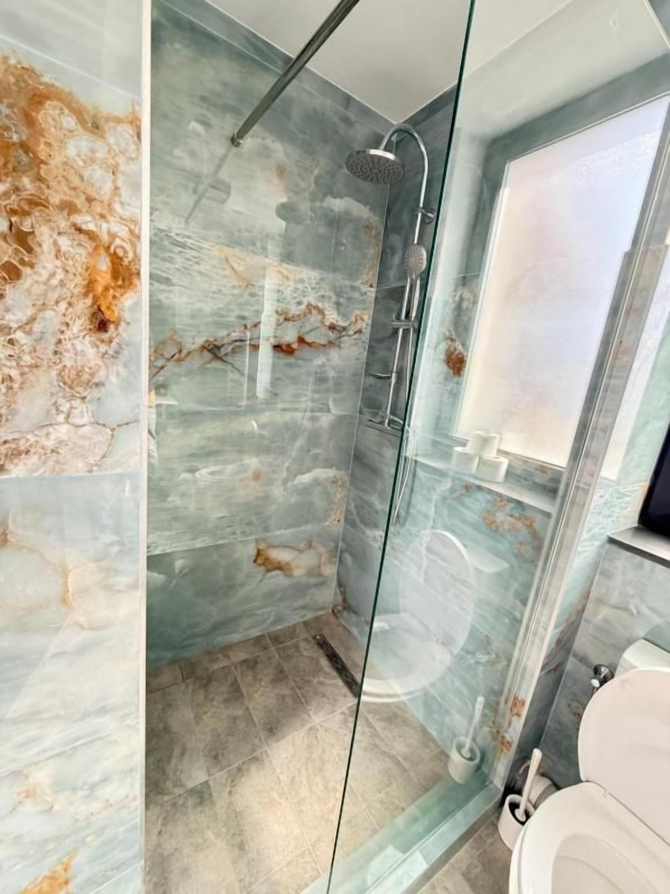 Une salle de bain moderne avec une douche à parois de verre, des murs en marbre et des toilettes.