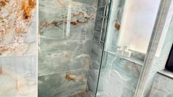 Une salle de bain moderne avec une douche à parois de verre, des murs en marbre et des toilettes.