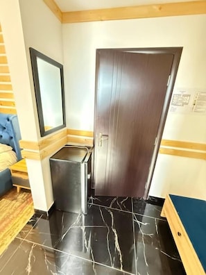 Una habitación con una puerta de madera oscura, un mueble negro pequeño, un espejo en la pared y un sofá azul.