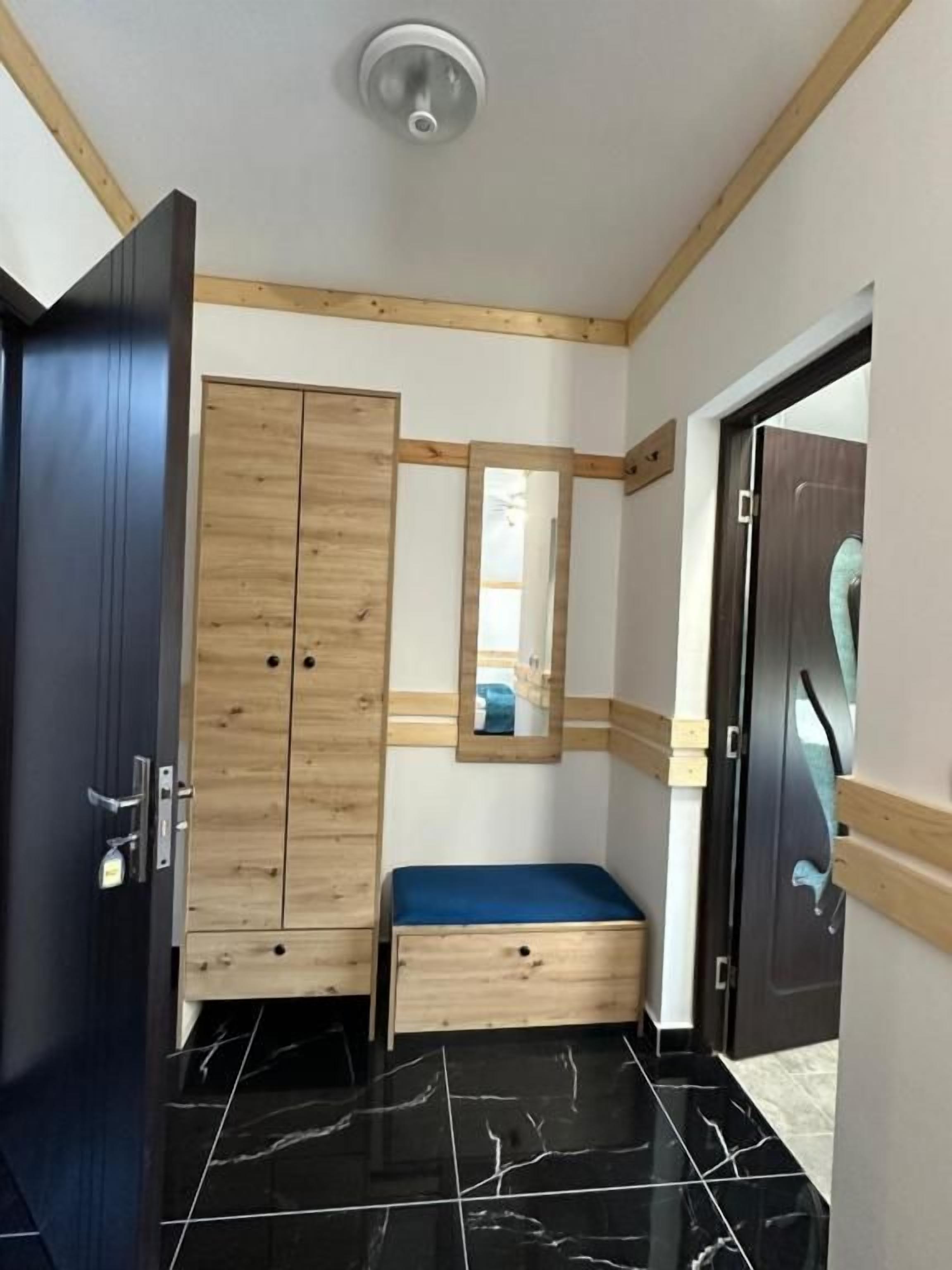 A room with a wooden wardrobe, a bench, a mirror, and a door.