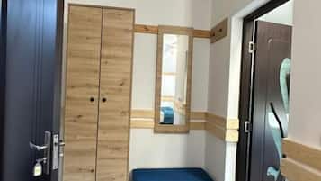 A room with a wooden wardrobe, a bench, a mirror, and a door.