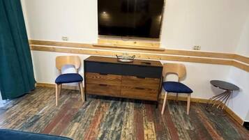 Une pièce avec un téléviseur fixé au mur, une commode en bois, deux chaises et un tapis à motifs.