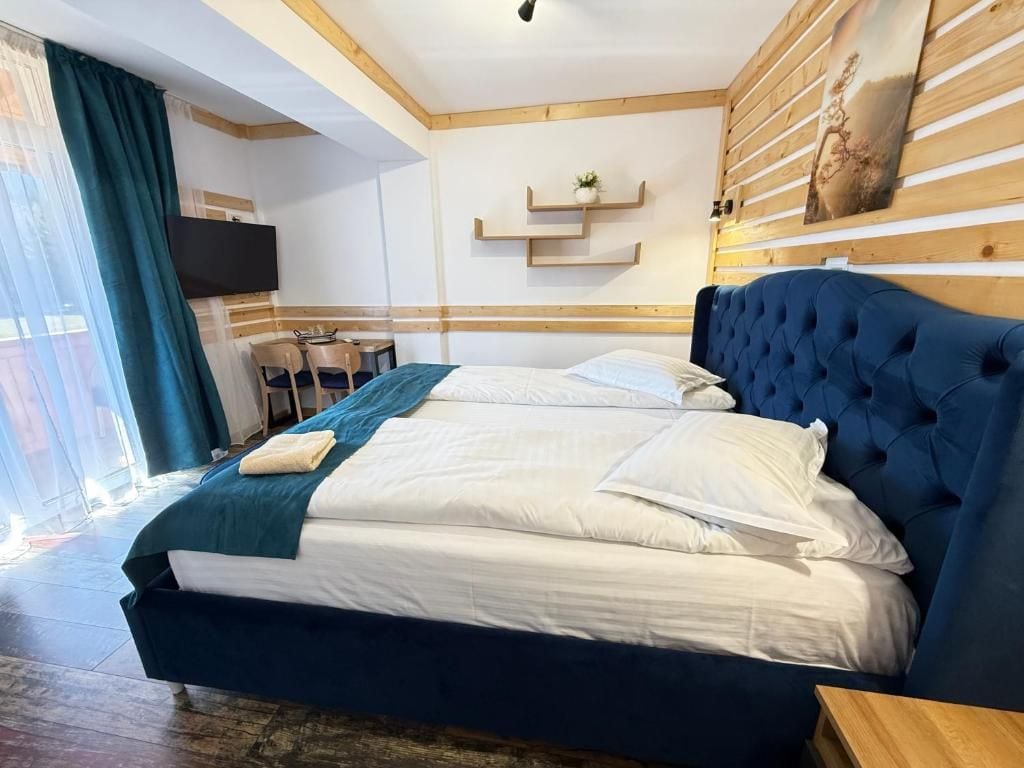 Hotellihuone, jossa on suuri sänky, seinälle asennettu televisio sekä ruokailutila, jossa on tuoleja ja pöytä.