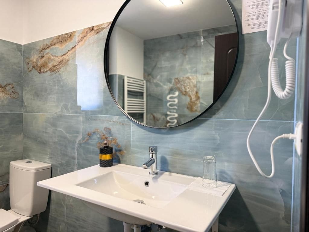 A bathroom with a white sink, a round mirror, and a toilet.