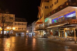 Ein belebter Stadtplatz bei Nacht mit Außenbestuhlung, einem Restaurant und einem Gebäude mit dem Schild 'P4'.
