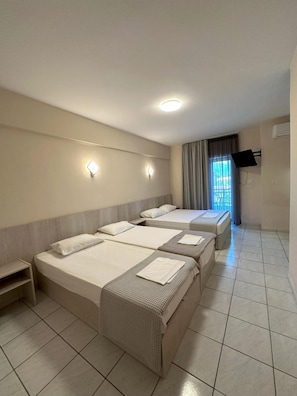 A hotel room with four beds, a flat-screen TV mounted on the wall, and a window with curtains. - Hotel Afroditi (Dio-Olympos)