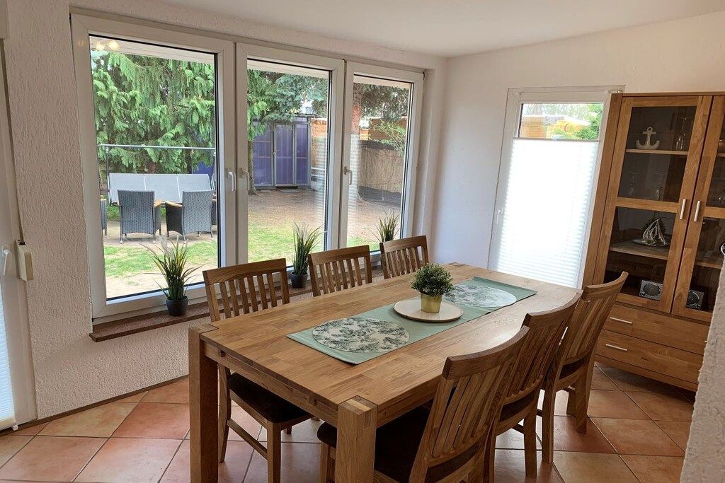 Un coin repas avec une table et des chaises en bois, une vitrine et une vue sur le jardin à travers de grandes portes-fenêtres coulissantes.