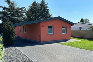 Ein eingeschossiges Gebäude mit flachem Dach, einer kleinen Veranda und einem gepflasterten Auffahrt.