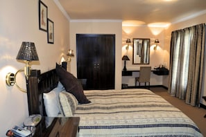 A hotel room with a bed, bedside lamps, a desk with a chair, a mirror, and a wardrobe. - Ipe Tombe Guest Lodge (Johannesburg)