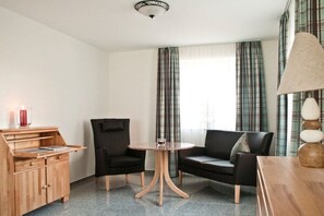 Ein Zimmer mit einem Holzkabinett, zwei Stühlen, einem runden Tisch und karierten Vorhängen.