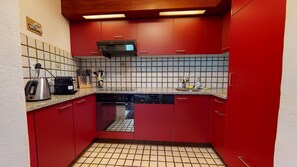 Eine kompakte Küche mit roten Schränken, einem Geschirrspüler, einer Kaffeemaschine und einer gefliesten Spritzschutzwand.