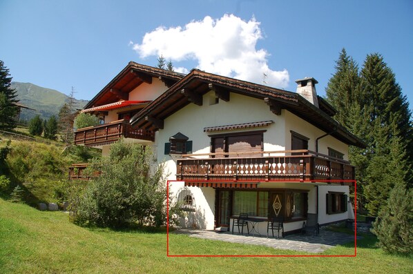 Ein zweistöckiges Chalet mit Balkon, einem Steinkamin und Blick auf den umliegenden Wald.