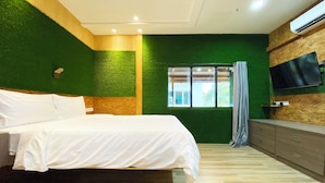 Une chambre à coucher avec un lit, une commode, un téléviseur fixé au mur et une fenêtre avec des rideaux.