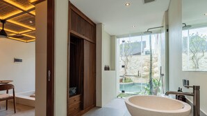 Un baño moderno con una bañera independiente grande, un box de ducha de vidrio y vistas a una piscina y jardín.