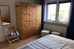 A bedroom with a bed, a wooden wardrobe, a chair, a window with curtains, and a radiator. - Holiday home with 3 bedrooms (Ostseebad Prerow)
