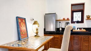 Una cocina con una mesa de madera, una silla, un refrigerador y un ventanal con un panel decorativo.