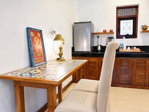 Una cocina con una mesa de madera, una silla, un refrigerador y un ventanal con un panel decorativo.