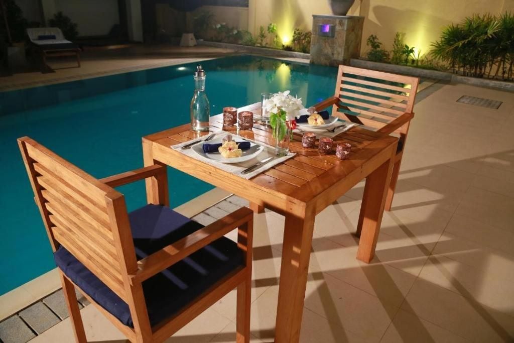 Una mesa de madera dispuesta con platos, cubiertos y vasos, cerca de una piscina.