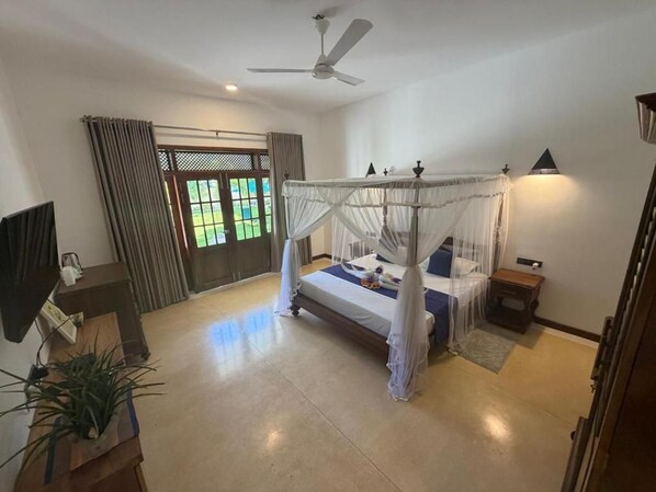 A bedroom with a four-poster bed, a ceiling fan, a bedside table, and a window with curtains.