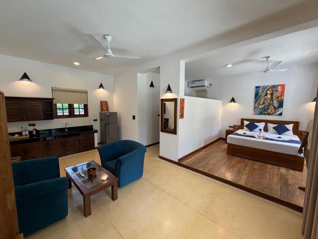 A modern hotel room with a kitchenette, a sofa, a dining table, and a bed.