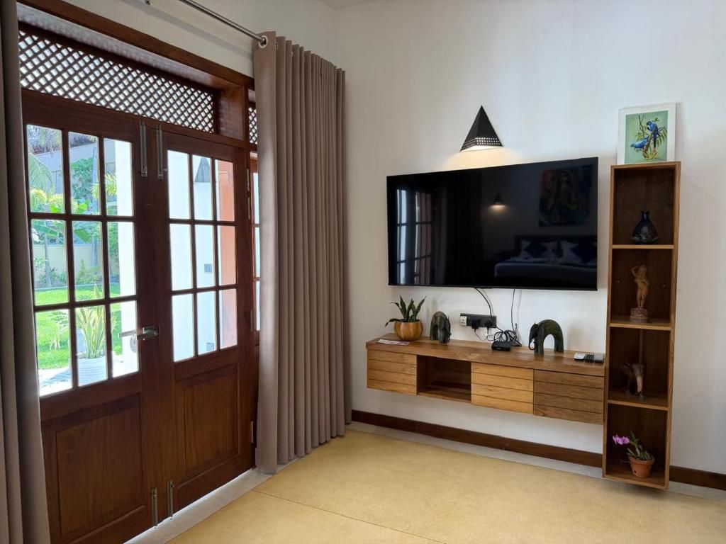 A living room with a TV mounted on the wall, wooden furniture, and a door with a view to the outside.