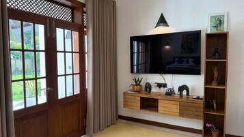 A living room with a TV mounted on the wall, wooden furniture, and a door with a view to the outside.