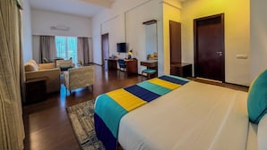 A hotel room with a large bed, a desk, a chair, a sofa, and a television. - Spree Resort at Century Wintersun (Bengaluru)
