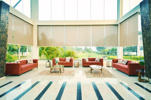 A spacious lobby with a large window, red sofas, a coffee table, and a rug. - Spree Resort at Century Wintersun (Bengaluru)