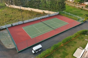 An outdoor tennis court with a red and green surface, surrounded by a white fence, and a golf cart parked nearby. - Spree Resort at Century Wintersun (Bengaluru)