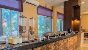 A breakfast bar with a variety of food items and containers, large windows with blinds, and a modern interior design. - Spree Resort at Century Wintersun (Bengaluru)