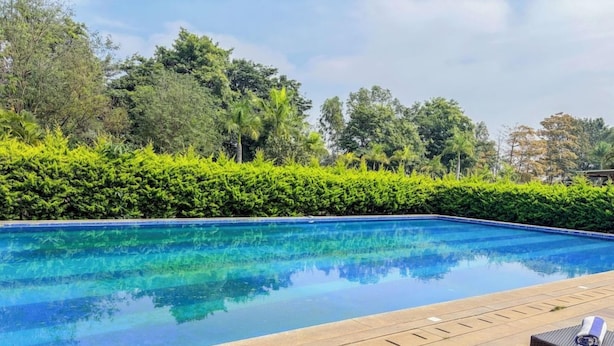 A clear swimming pool with lounge chairs and a neatly trimmed hedge. - Spree Resort at Century Wintersun (Bengaluru)